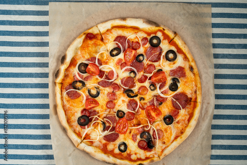 Top view of pizza with pepperoni, olives and tomato slices on craft paper on the table