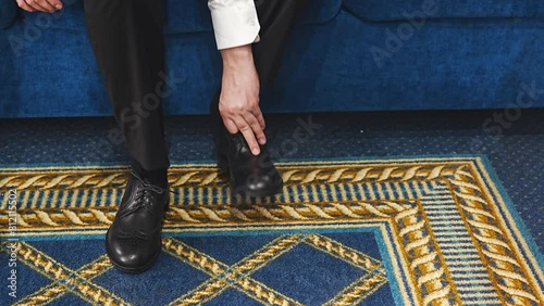 A man puts on black leather dress shoes. without a face. 