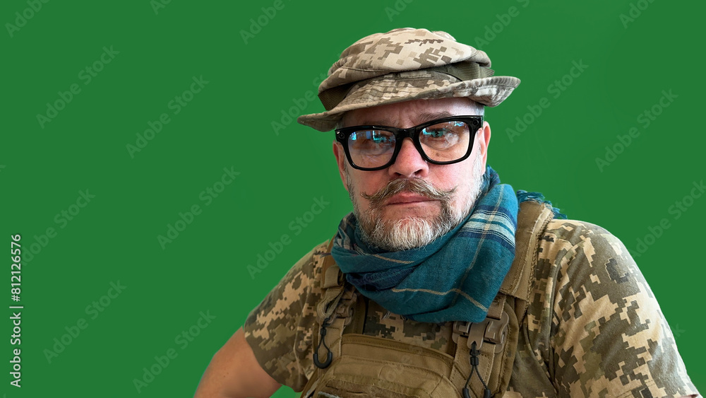 Fototapeta premium Portrait of an elderly Ukrainian soldier with moustache and glasses. In tactical hat, in bulletproof vest with scarf around his neck. War in Ukraine
