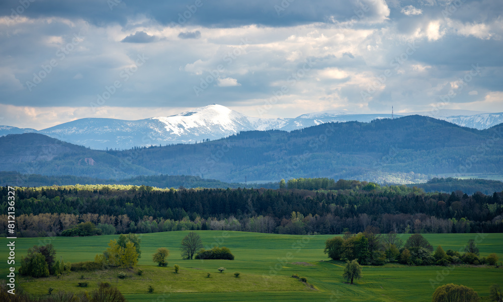 view on snowy summit of Sniezka mountain with spring green fields in Kaczawskie mountains