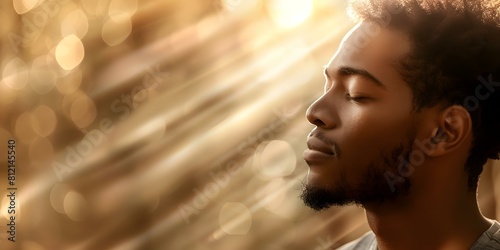 Young African American man praying with eyes closed divine light shining down. Concept Religious Imagery, African American, Spirituality, Prayer, Divine Light