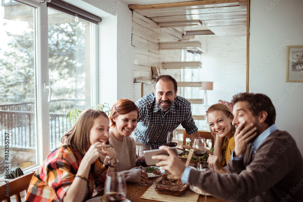 Friends taking a group selfie during a cozy winter meal indoors Friends taking a group selfie during a cozy winter meal indoors