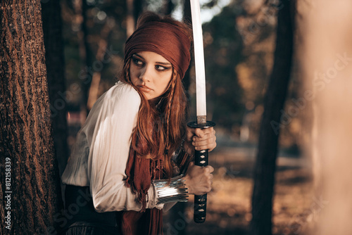 Outdoor portrait of young female in pirate costume holding a sword.