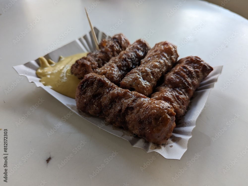 Mici cu mustar and a toothpick on a paper plate. Traditional romanian fast food.