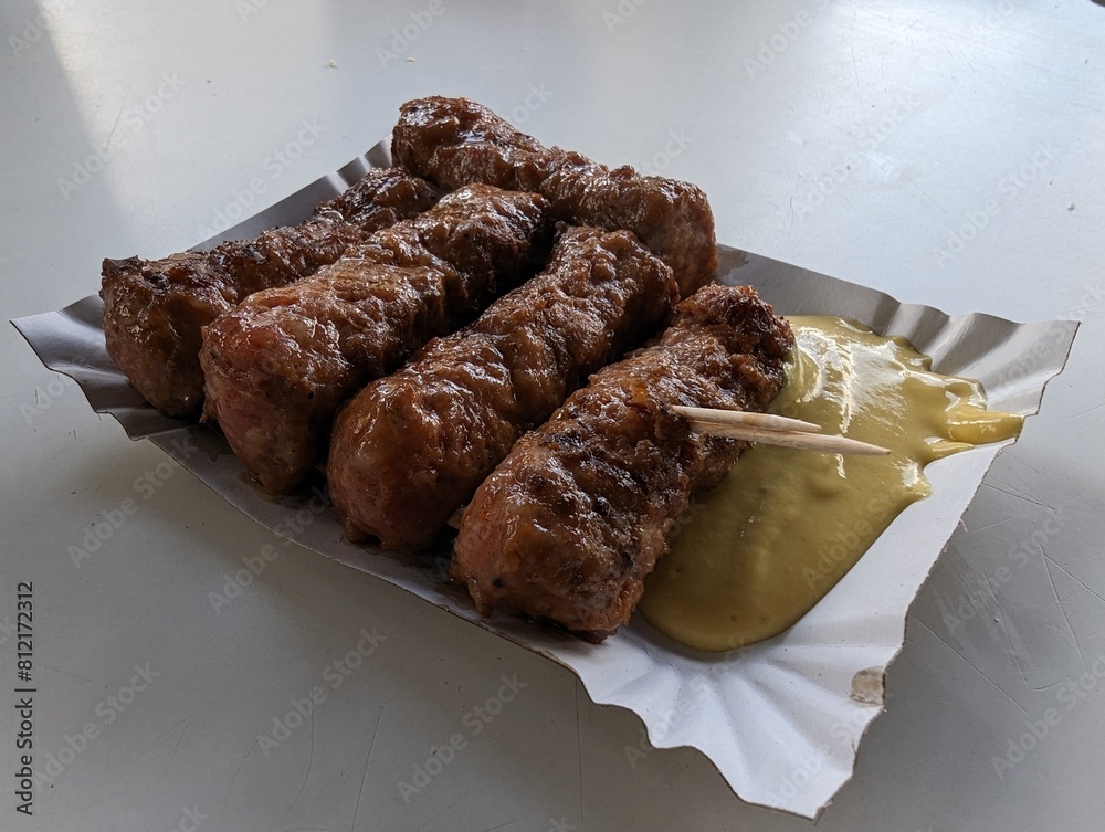 Mici cu mustar and a toothpick on a paper plate. Traditional romanian fast food.