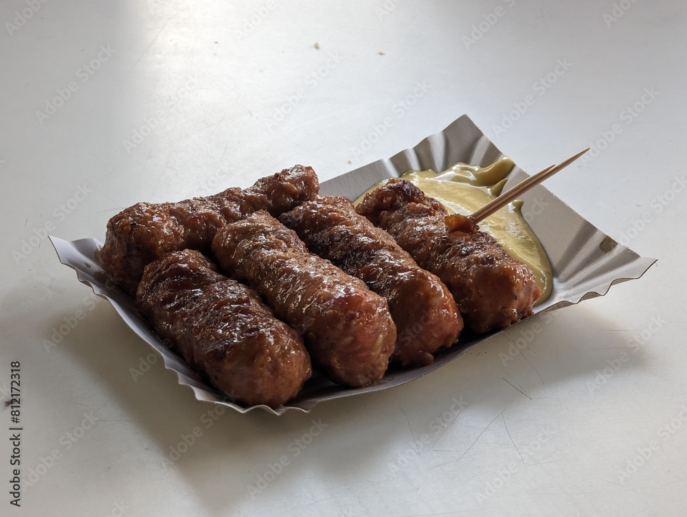 Mici cu mustar and a toothpick on a paper plate. Traditional romanian fast food.