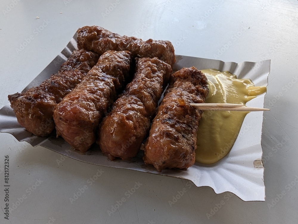 Mici cu mustar and a toothpick on a paper plate. Traditional romanian fast food.