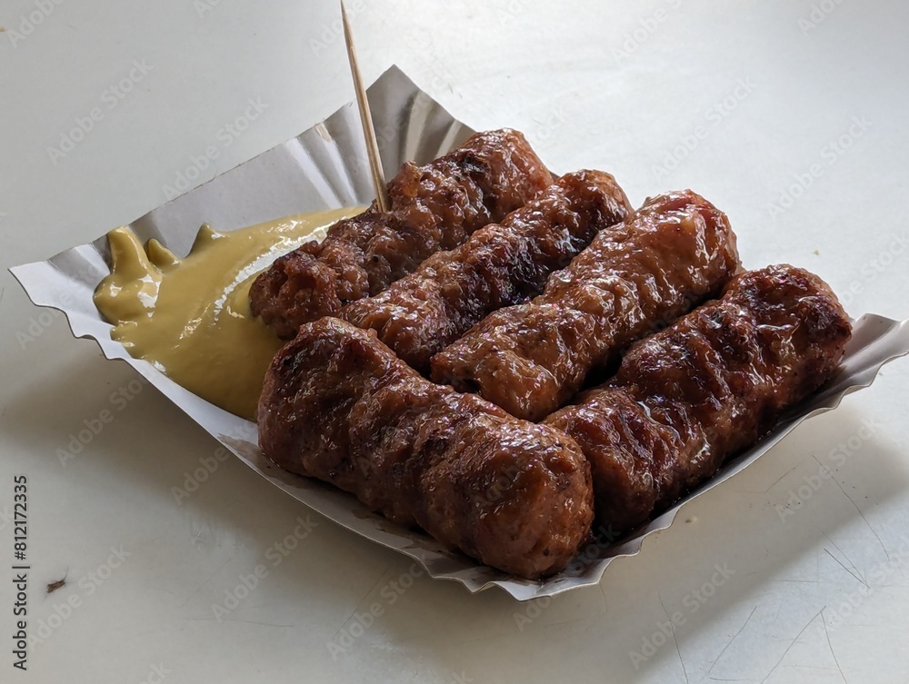 Mici cu mustar and a toothpick on a paper plate. Traditional romanian fast food.