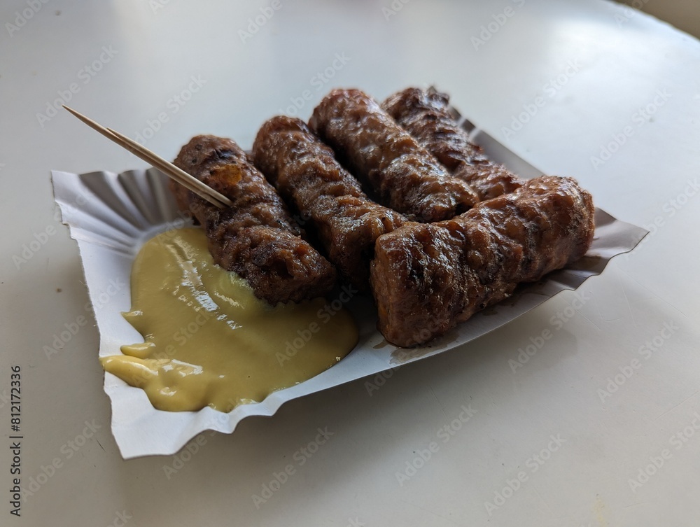Mici cu mustar and a toothpick on a paper plate. Traditional romanian fast food.