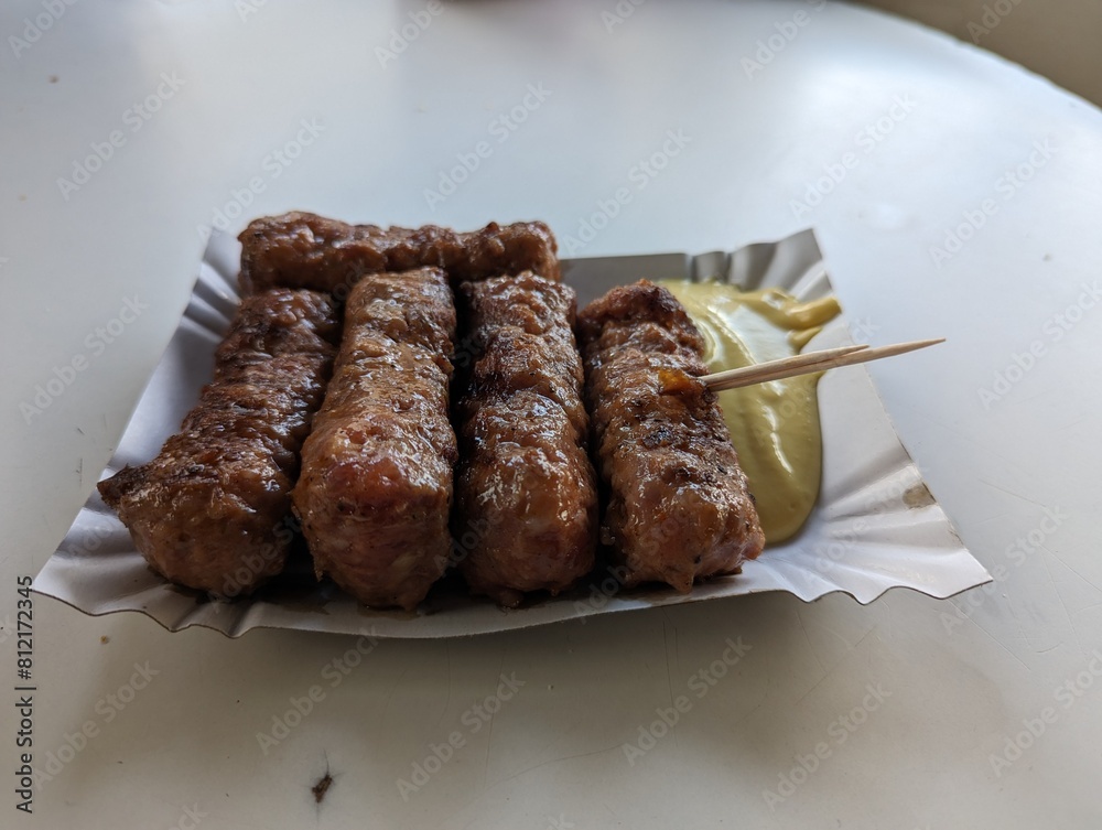 Mici cu mustar and a toothpick on a paper plate. Traditional romanian fast food.