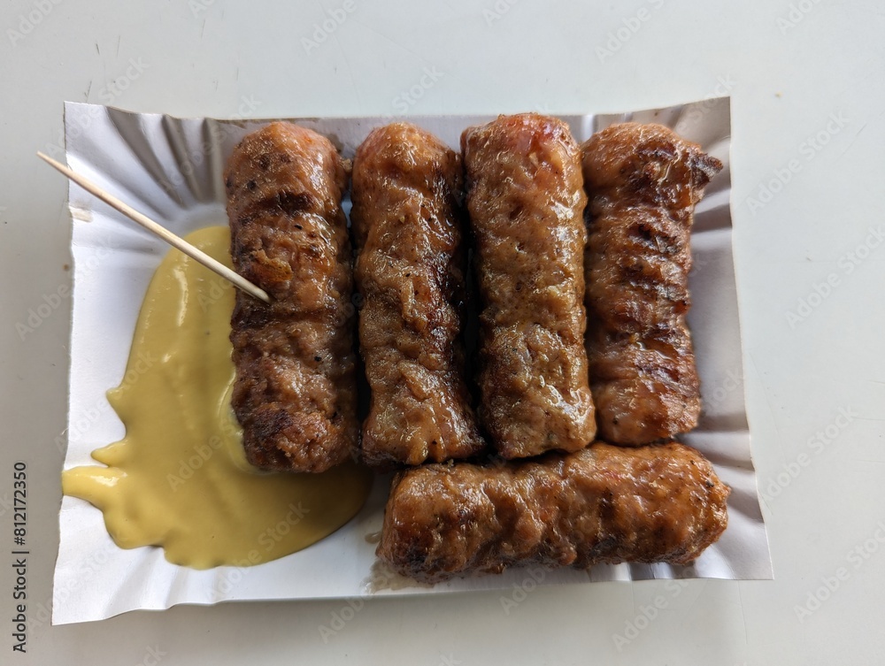 Mici cu mustar and a toothpick on a paper plate. Traditional romanian fast food.