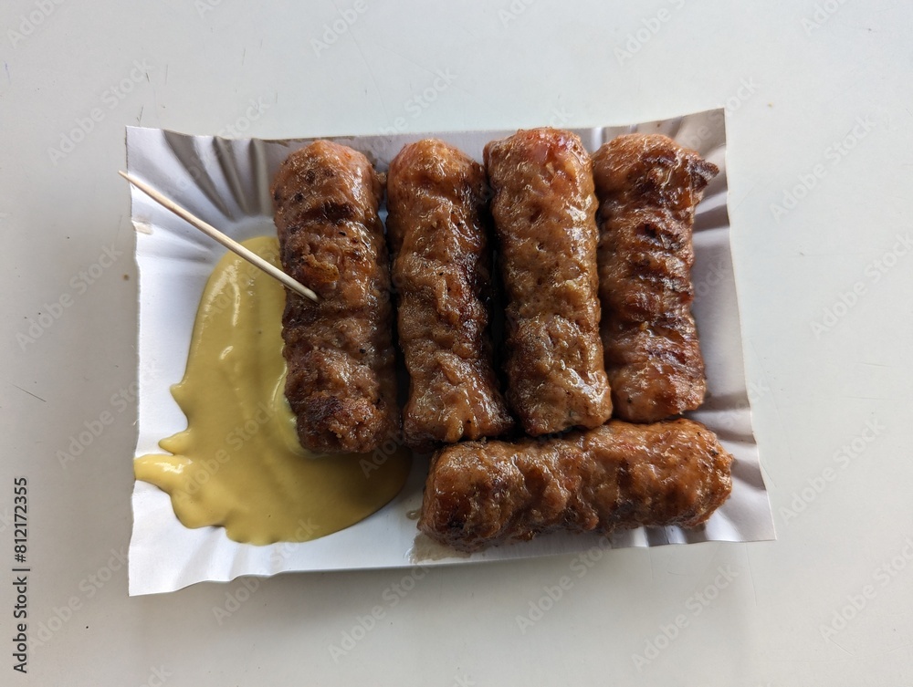 Mici cu mustar and a toothpick on a paper plate. Traditional romanian fast food.