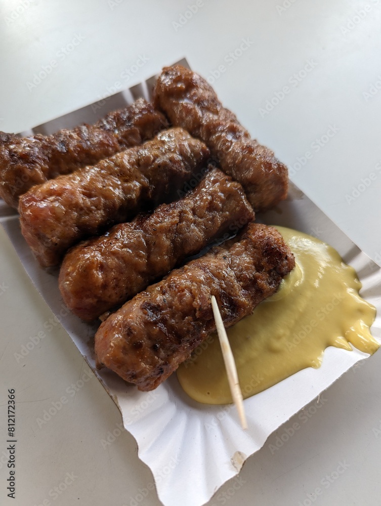 Mici cu mustar and a toothpick on a paper plate. Traditional romanian fast food.