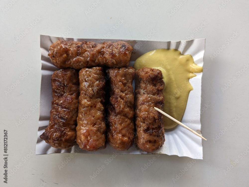 Mici cu mustar and a toothpick on a paper plate. Traditional romanian fast food.