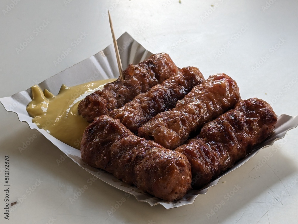 Mici cu mustar and a toothpick on a paper plate. Traditional romanian fast food.