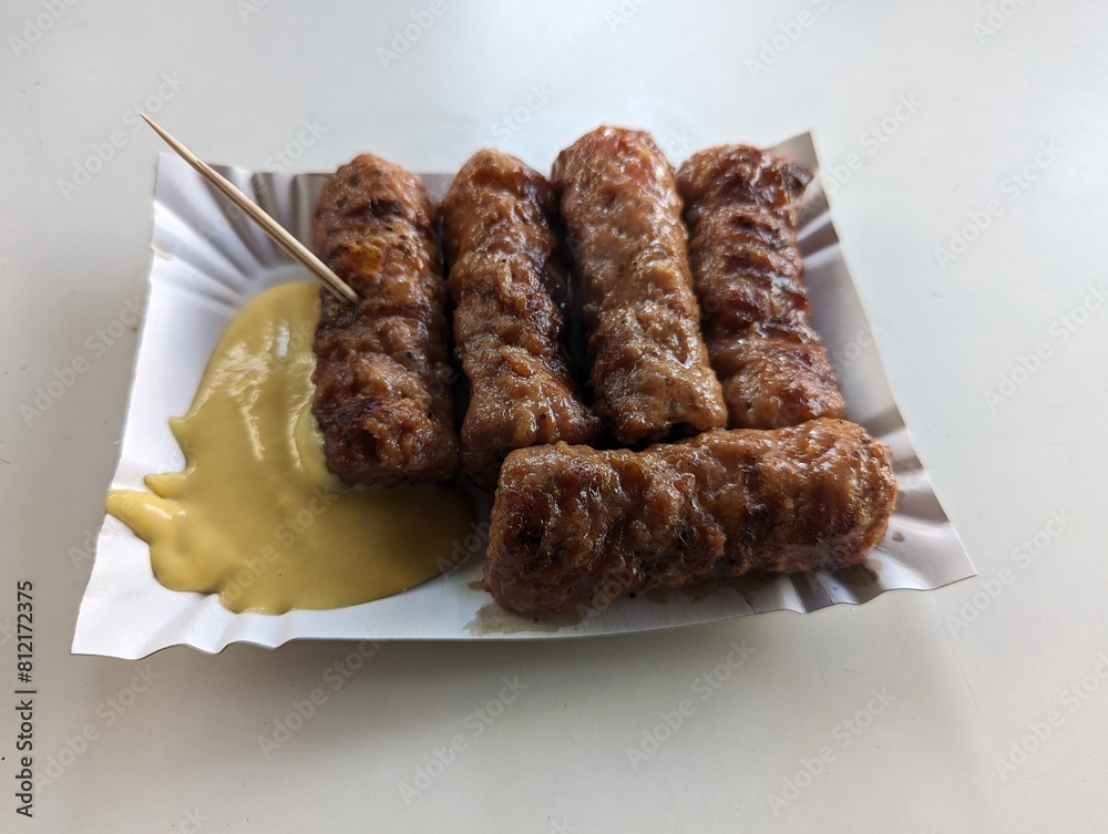 Mici cu mustar and a toothpick on a paper plate. Traditional romanian fast food.