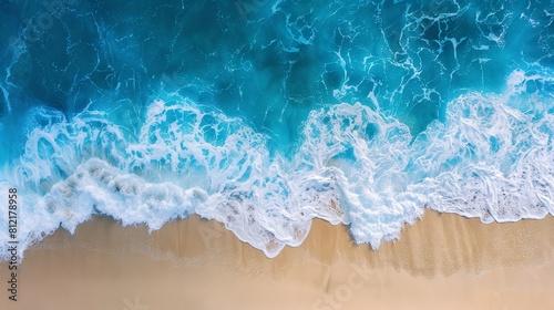 Aerial top-down view of ocean waves crashing onto a sandy beach, capturing the essence of summer vacation with vibrant blue waters