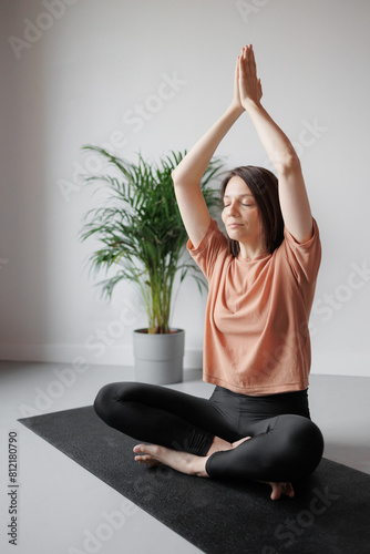 Caucasian woman meditates in lotus position, hands above head, with her eyes closed at home. Spiritual, physical practices for mental health. Sports recreation. happy Person coaching, stretching.