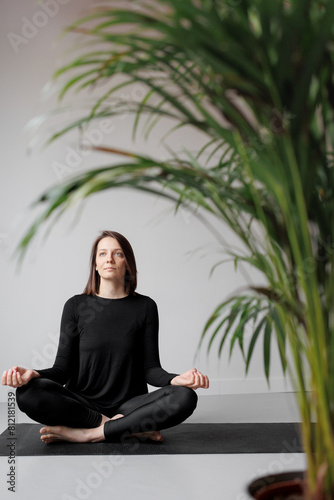 person in black clothes meditates with his eyes closed in lotus namaste pose, practicing yoga. Taking care of body and mental health. A female yoga teacher. Harmony, balance and healthy lifestyle