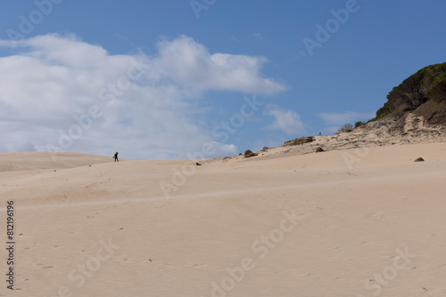 People walking up sand dunes hiking on a bright sunny day © Barosanu