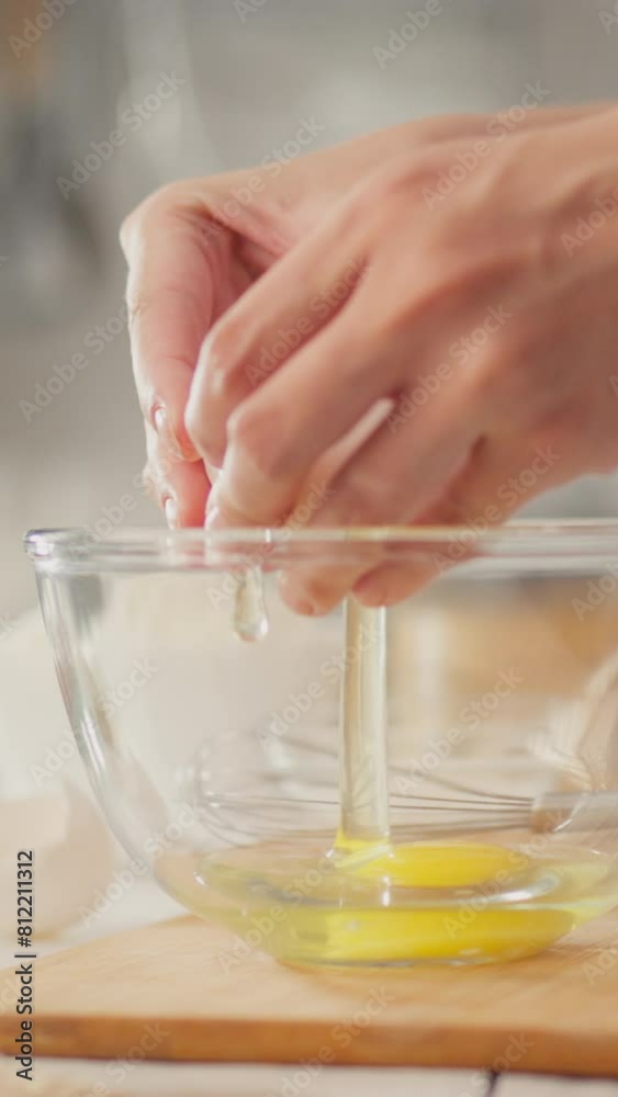 Vertical position. A young woman breaks a yellow egg in a modern kitchen. The camera captures how a housewife carefully cracks an egg into a plate while experimenting with new pancake recipes Vertical position. A young woman breaks a yellow egg in a modern kitchen. The camera captures how a housewife carefully cracks an egg into a plate while experimenting with new pancake recipes