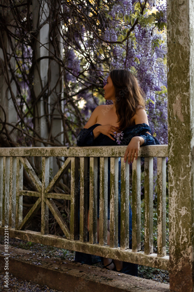 Attractive woman in blue dress near blooming wisteria. Ancient building Attractive woman in blue dress near blooming wisteria. Ancient building