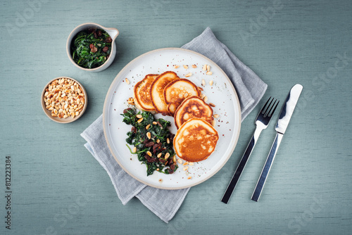 Traditional American pancakes with spinach, pine-nuts and raisins served as top view on a Nordic design plate with cutlery photo