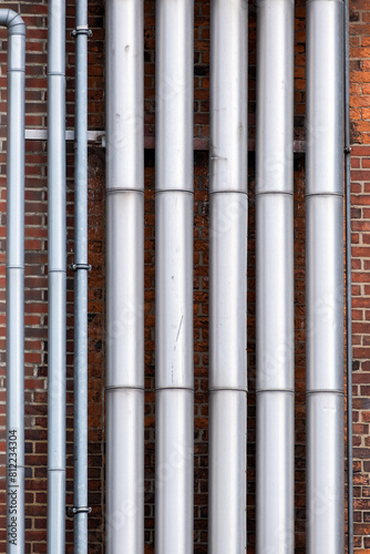 Large and smaller silver pipes on a house wall with red bricks.