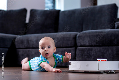 Cute young woman is sleeping on sofa in living room while little child is playing with robot vacuum cleaner on floor at home.