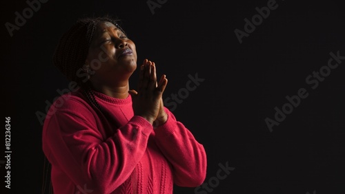 Graceful black woman gazing upwards with palms extended in gesture of reverance and adoration. Side-view portrait of african american lady engaged in prayerful reflection in isolated background. photo