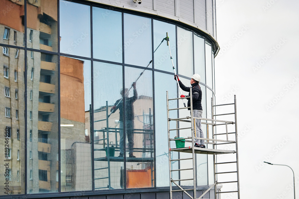 Worker on scaffold washes glass facade of business center. Window