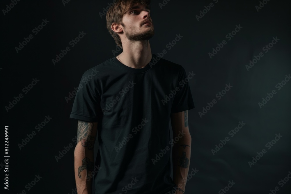 Young male with tattoos, looking away thoughtfully, isolated on a dark backdrop
