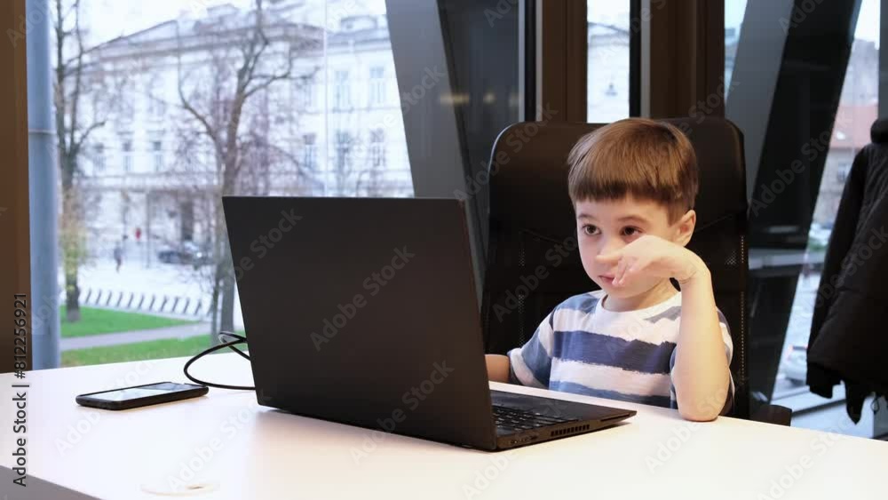 Attentive 6 year boy using laptop in office looking at screen. The child rubs his eyes. Dry eye syndrome concept. Distance education. Programming lesson. Concentrated child solves difficult task Attentive 6 year boy using laptop in office looking at screen. The child rubs his eyes. Dry eye syndrome concept. Distance education. Programming lesson. Concentrated child solves difficult task