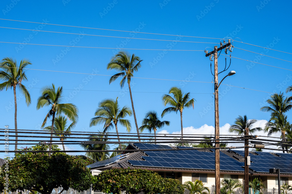 Condo building roof covered in solar panels to generate green alternative energy on sunny Maui, in contrast to the utility power distribution lines in front
