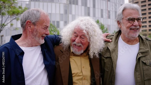 Group of three mature caucasian men enjoying embracing walk together laughing outdoor. Senior male old friends having fun hugging strolling happy in the urban city street. Elderly people golden ager photo