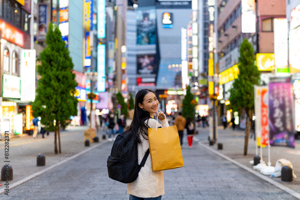 Happy Asian woman holding shopping bag walking at Shibuya district, Tokyo, Japan in evening. Attractive girl enjoy and fun outdoor lifestyle travel urban city street and shopping on holiday vacation.