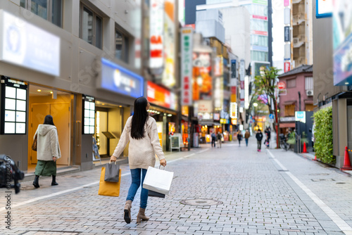 Happy Asian woman holding shopping bag walking at Shibuya district, Tokyo, Japan in evening. Attractive girl enjoy and fun outdoor lifestyle travel urban city street and shopping on holiday vacation. photo