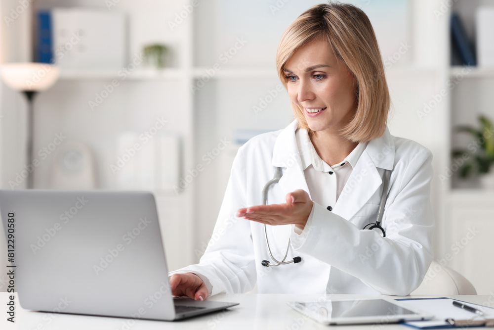 Smiling doctor with laptop having online consultation at table in office Smiling doctor with laptop having online consultation at table in office