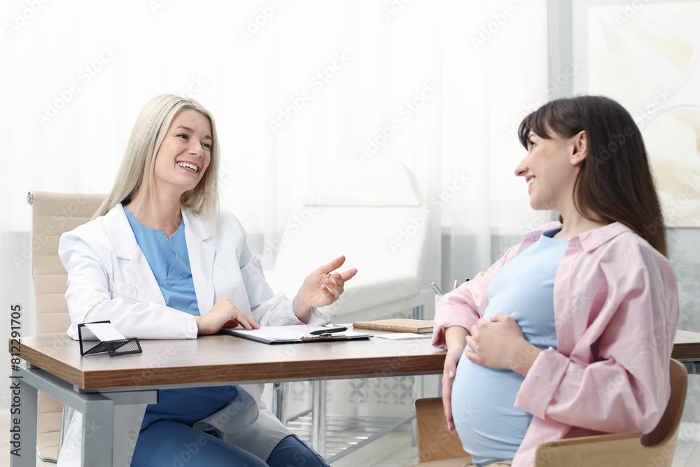 Smiling doctor consulting pregnant patient at table in clinic Smiling doctor consulting pregnant patient at table in clinic