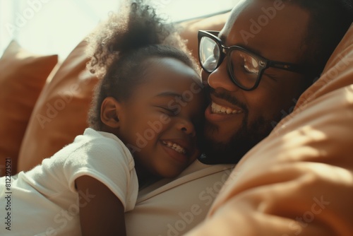 Heartwarming image capturing an affectionate embrace between a smiling father with glasses and his young daughter, sharing a joyous moment together on a cozy, sunlit bed