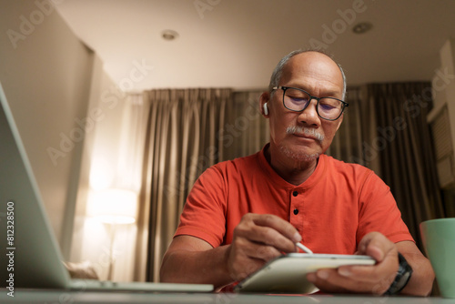 Senior Asian businessman focused on work, using laptop and taking notes at home office