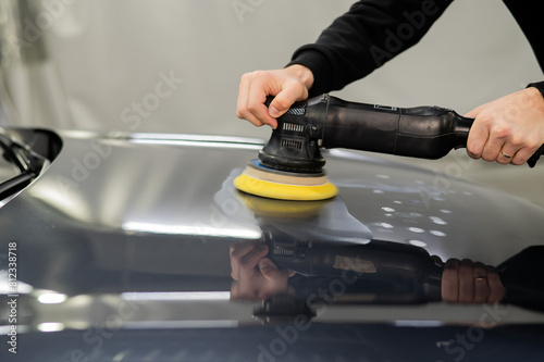 A mechanic polishes the surface of the hood of a gray car. 