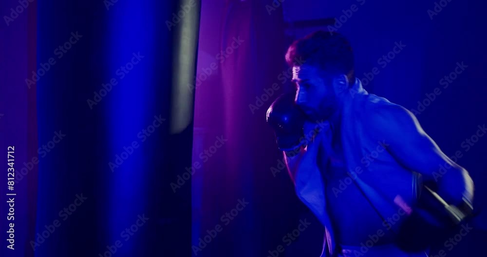 Man Punching Punching Bag in Dark Neon-lit Room Man Punching Punching Bag in Dark Neon-lit Room