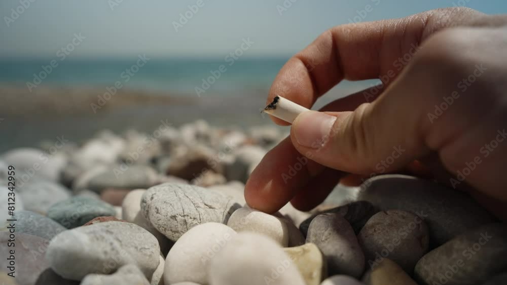 A man's hand holds cigarette remnants against the backdrop of the sea, he throws it onto the rocks, environmental pollution. Smoking cessation. A man's hand holds cigarette remnants against the backdrop of the sea, he throws it onto the rocks, environmental pollution. Smoking cessation.