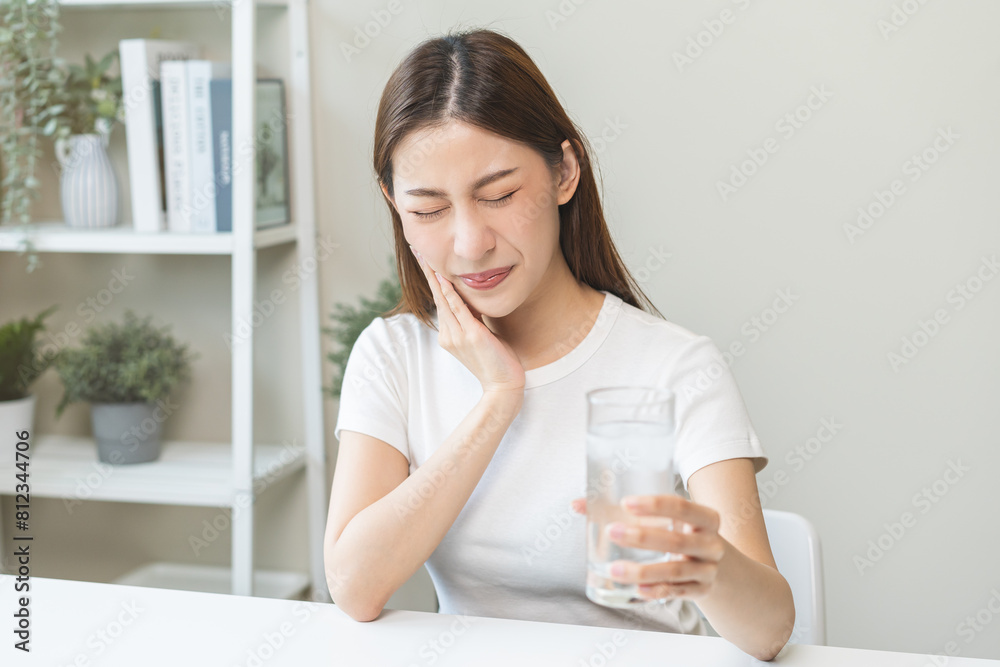 Suffering from toothache, blur asian young woman touch cheek, face expression ache or feel pain, sensitive molar teeth, hand holding glass of water with ice, inflammation when drink cold, healthcare. Suffering from toothache, blur asian young woman touch cheek, face expression ache or feel pain, sensitive molar teeth, hand holding glass of water with ice, inflammation when drink cold, healthcare.
