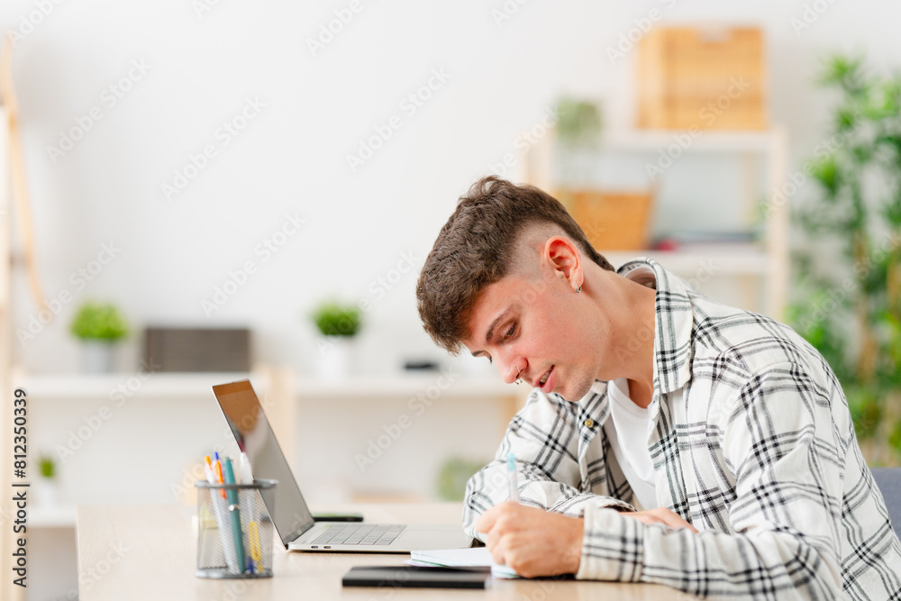 Young man writing ideas during an online class sitting on the living room Young man writing ideas during an online class sitting on the living room