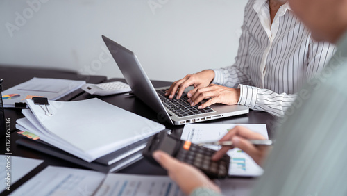 Two business real estate seller using calculator to calculating and discussion about property investment while typing terms data about home sales contract and home insurance on laptop in office