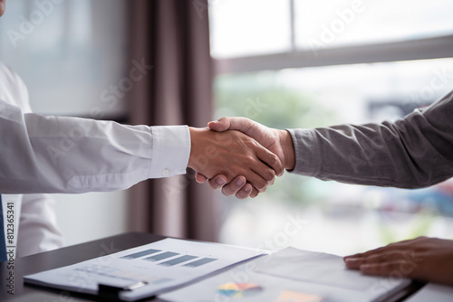Businessman real estate seller and business shaking hands together after reading property investment document to discussion about deal agreement terms data of home sales contract and home insurance