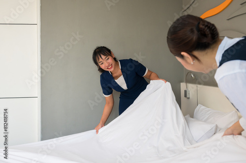 Hotel room service. Young two Asian woman maid in uniform making bed in guest room