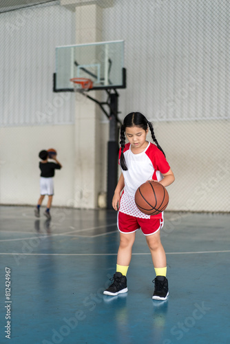 basketball by asian child or kid girl fun playing and training to learning bouncing and raising ball by left hand with children at sports stadium school or basketball court for exercise sport holiday